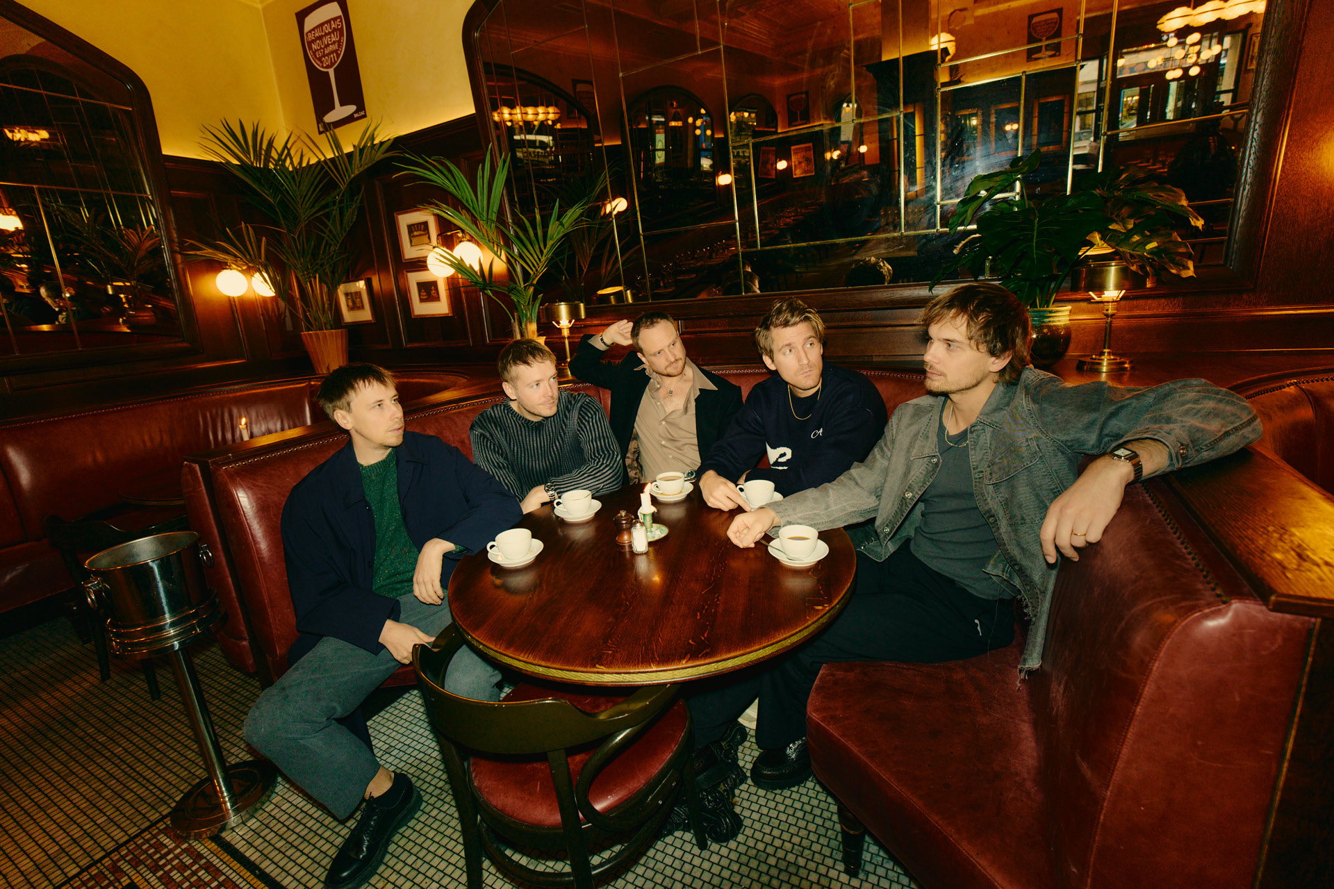 Bandet Tjuvjakt, fem killar, sitter runt ett bord i restaurangmiljö. Mörka trädetaljer och skinnsoffor.